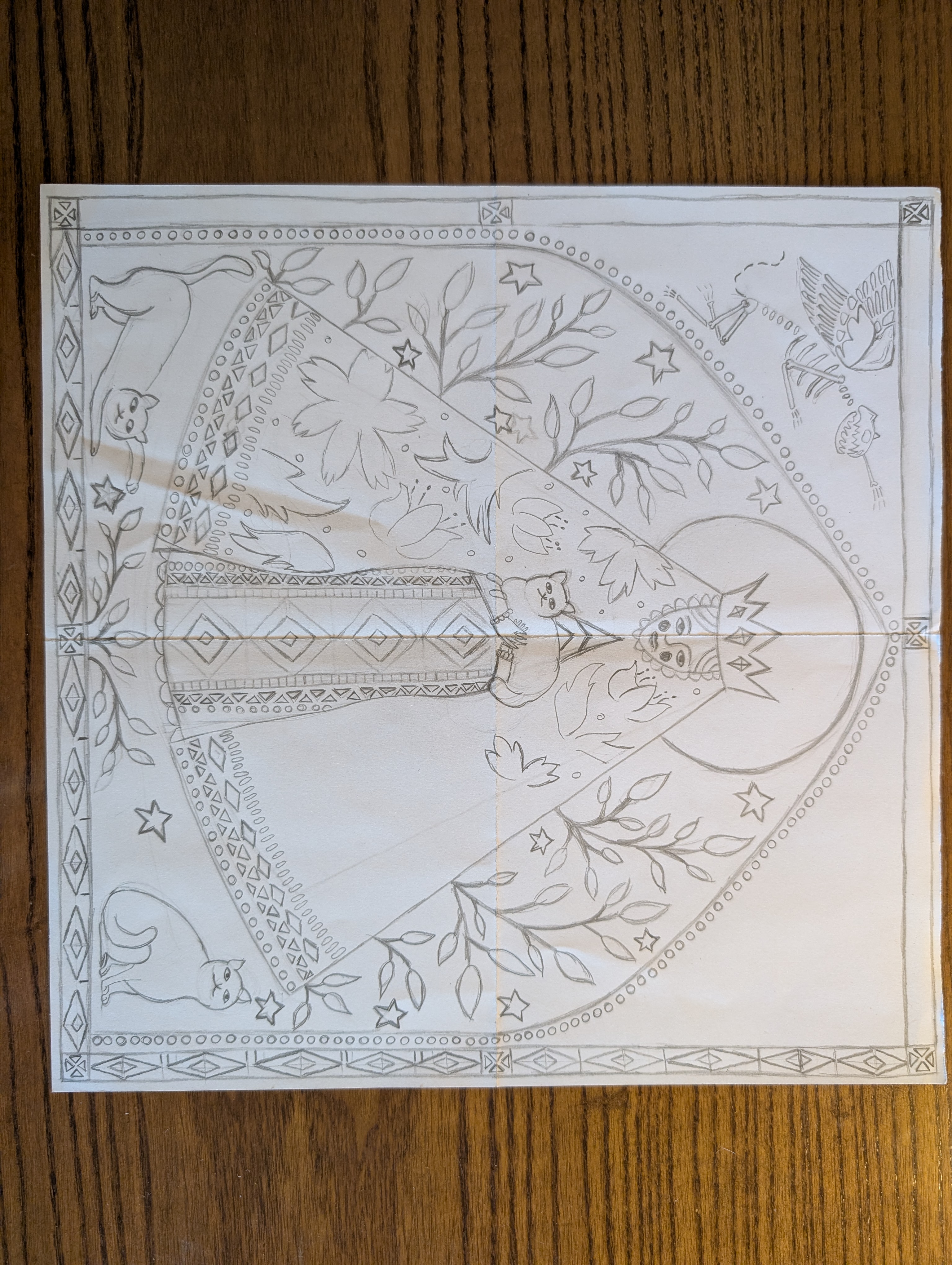 A pencil sketch of an in-progress A3 linocut composition inspired by medieval and folk art. The central figure is a crowned woman framed by a large halo, surrounded by stylized birds, flowers, foliage, stars, and three cats. Decorative geometric borders and a Gothic-inspired arch frame the scene, with the symmetrical design carefully planned before carving. The photograph documents the initial drawing stage of the printmaking process.
