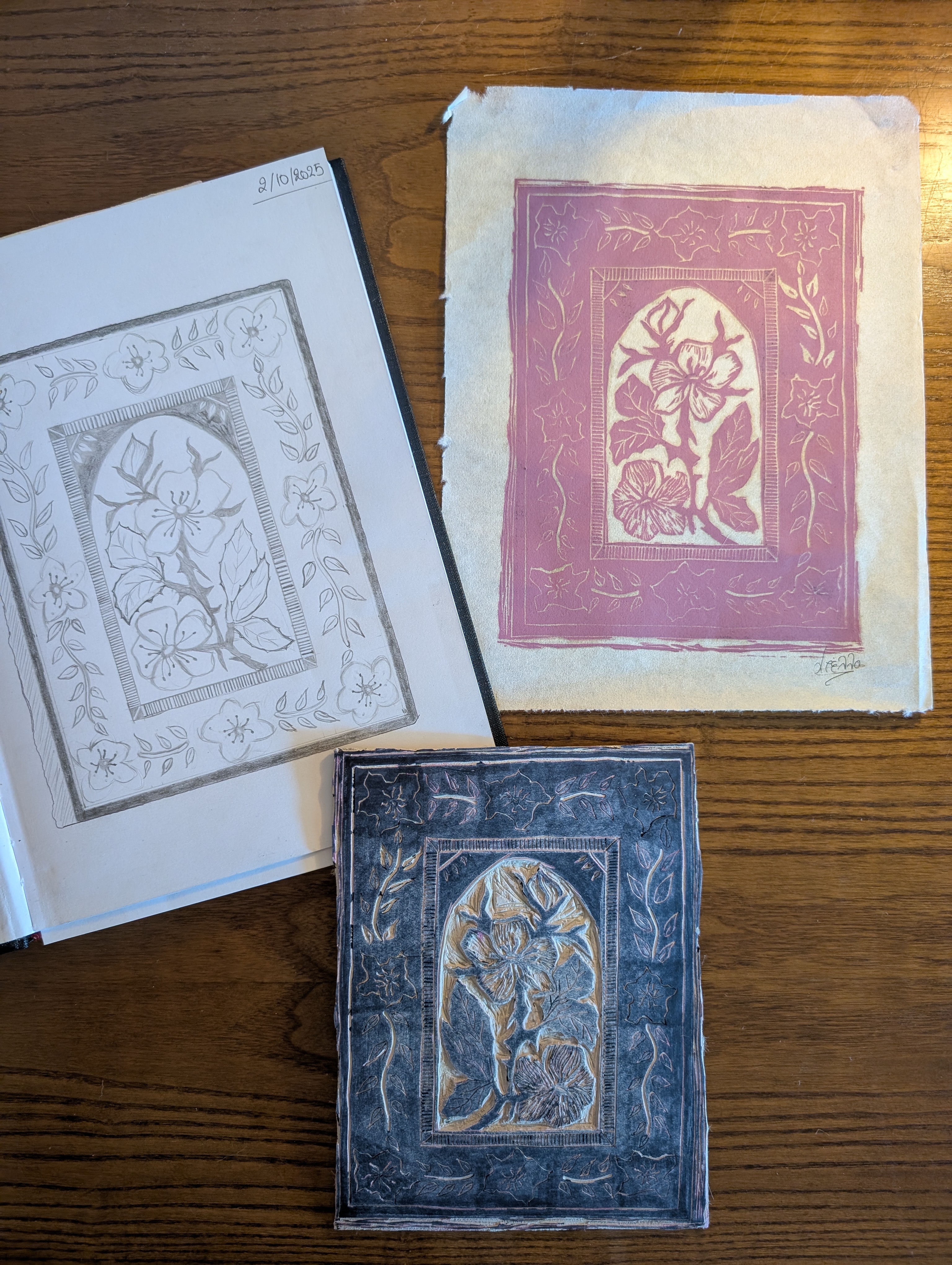 A process photo documenting the creation of a floral linocut print. The image includes the original pencil sketch, the completed print in a muted pink ink, and the hand-carved linoleum block used to produce it. The decorative composition features a blooming flower surrounded by an ornate botanical border, highlighting the transformation from concept sketch to carved block and finished handmade print.